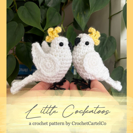 Two crochet cockatoos held in hands with a plant in the background, featuring a crochet pattern by 'CrochetCartelCo'.