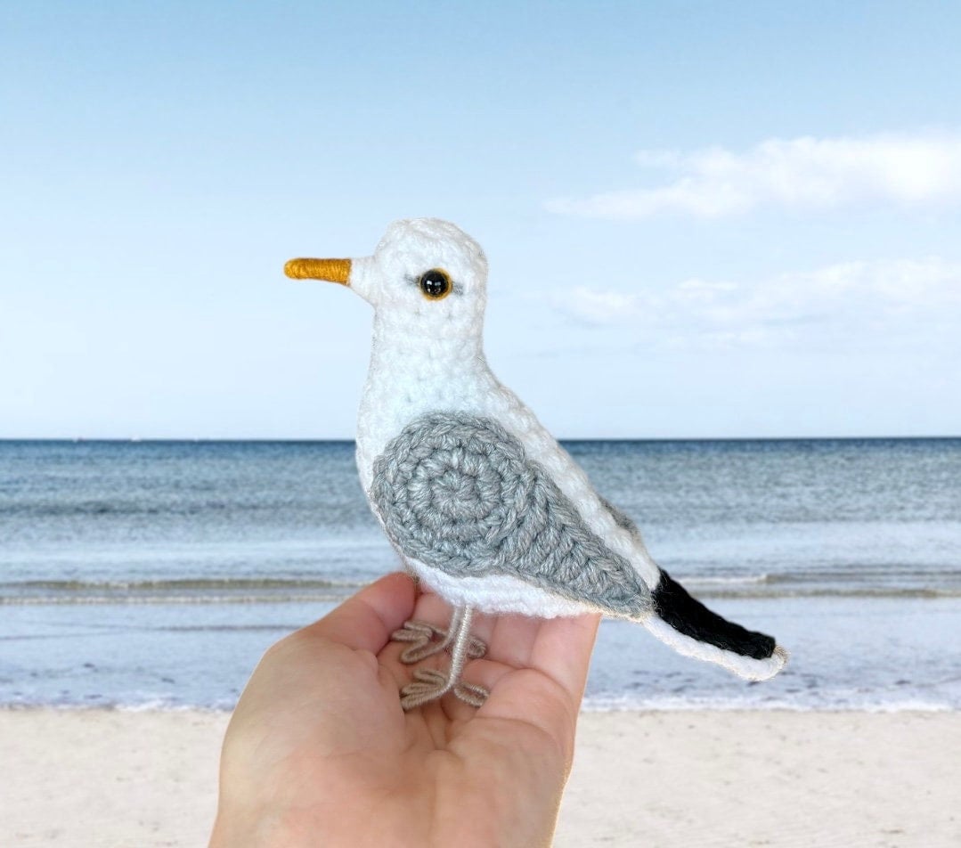 Hand holding a crochet seagull toy with a beach background