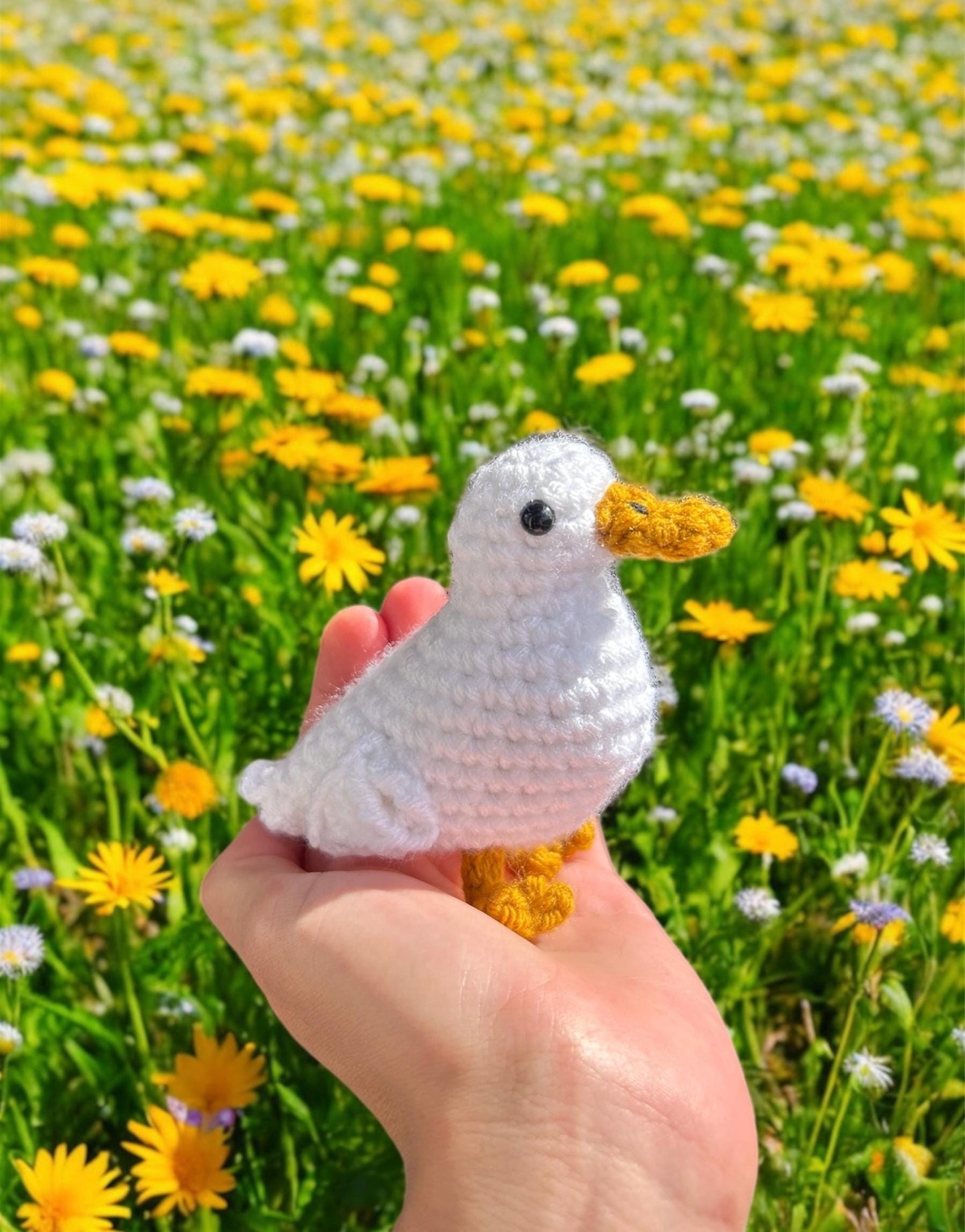 Hand holding a small crochet duck in front of a field of yellow flowers