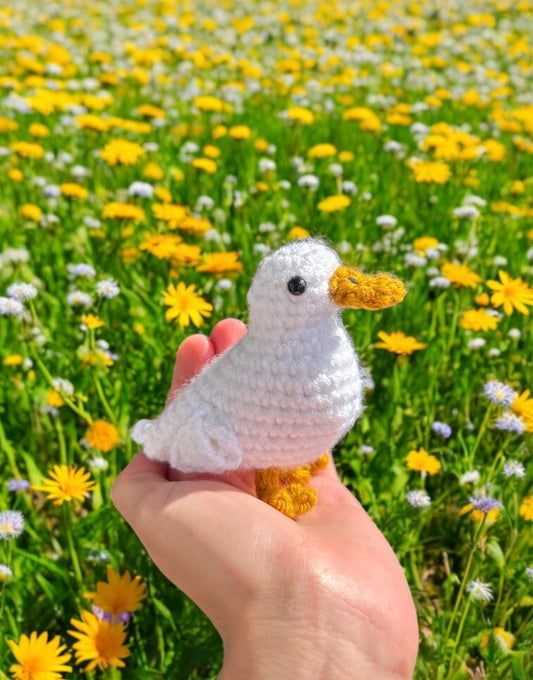 Hand holding a small crochet duck in front of a field of yellow flowers
