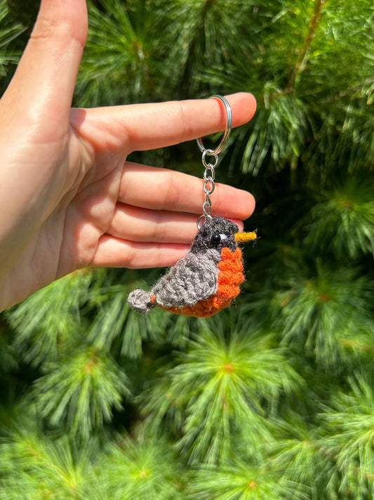 Hand holding a crocheted bird keychain with a green foliage background