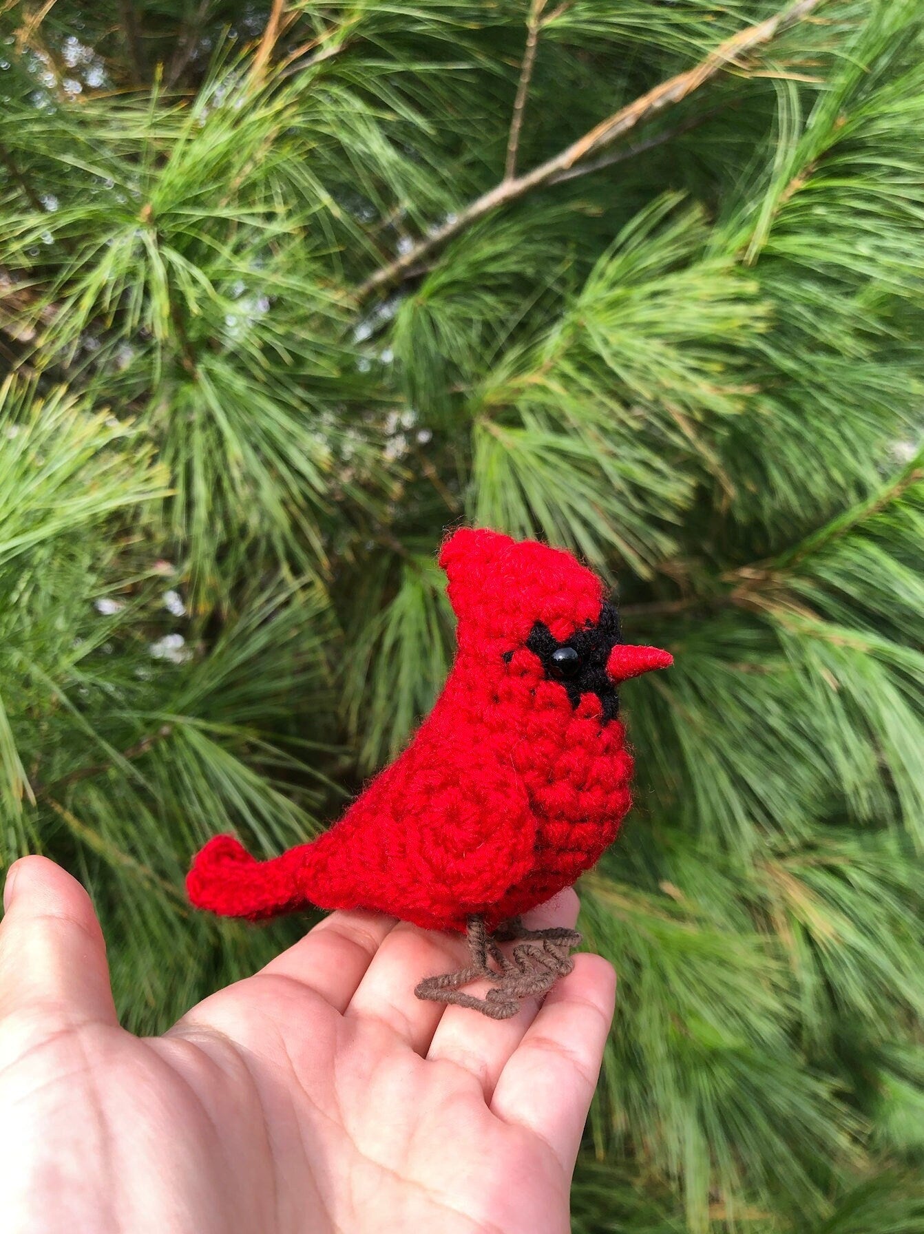 Red crochet cardinal held in a hand with a green leafy background