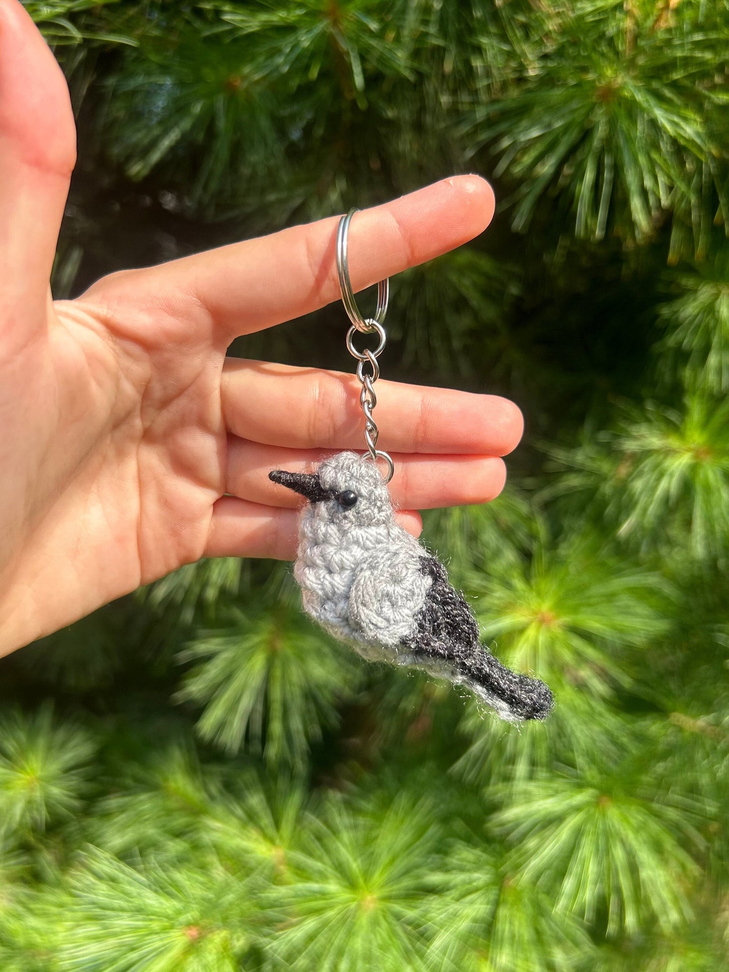 Hand holding a crocheted bird keychain against a green foliage background