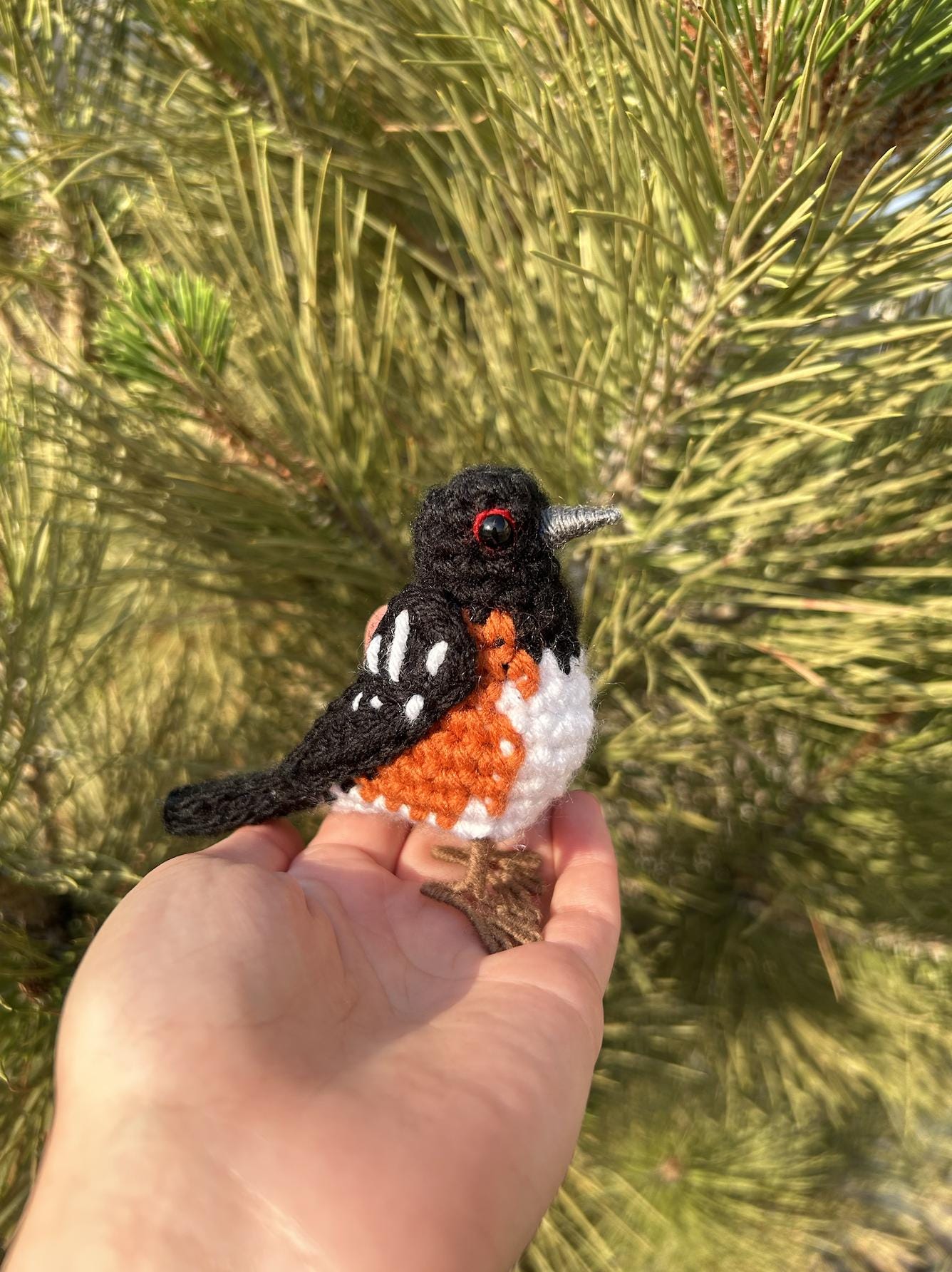 Hand holding a small crocheted bird against a natural background