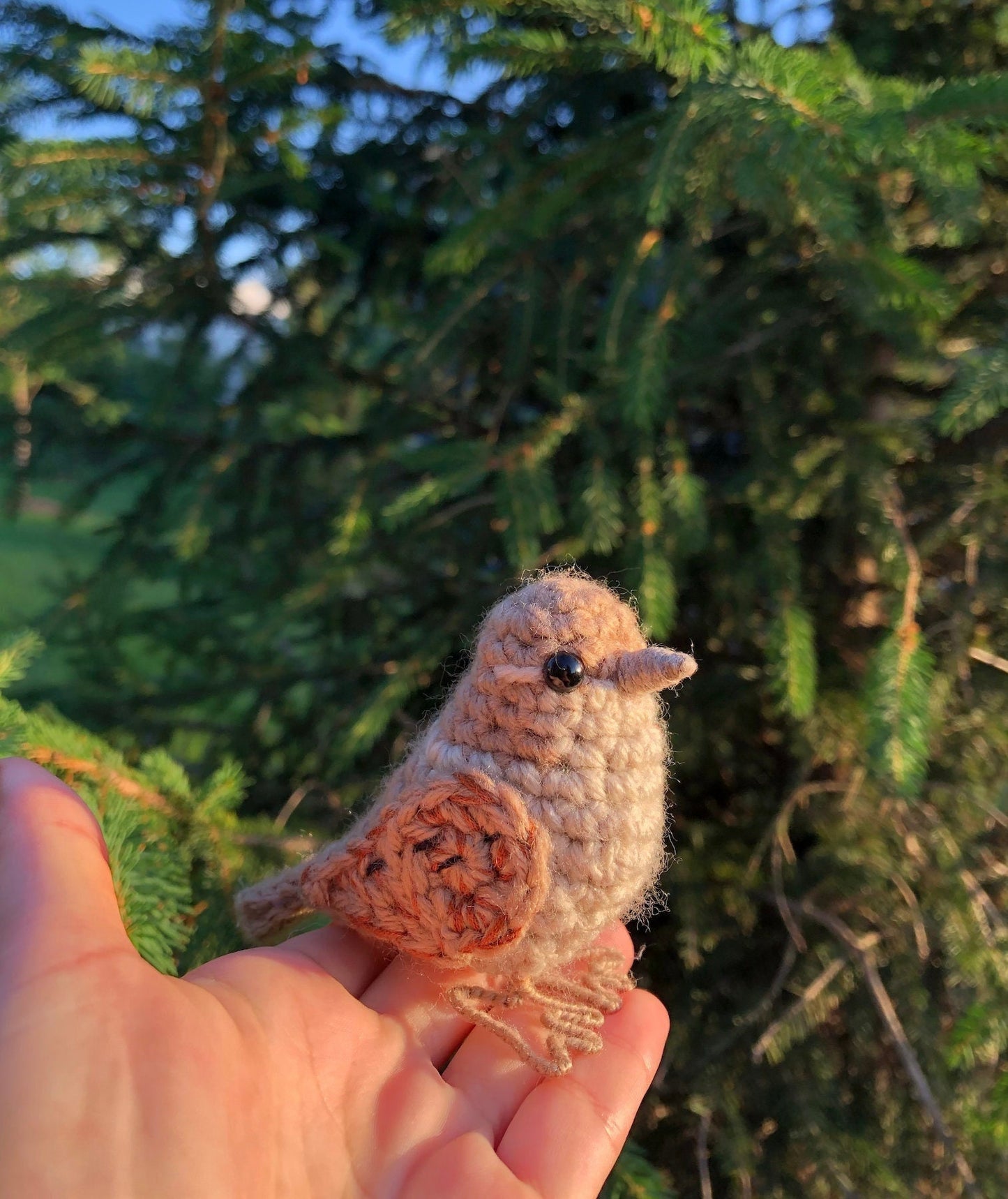 Hand holding a small crocheted bird against a green leafy background