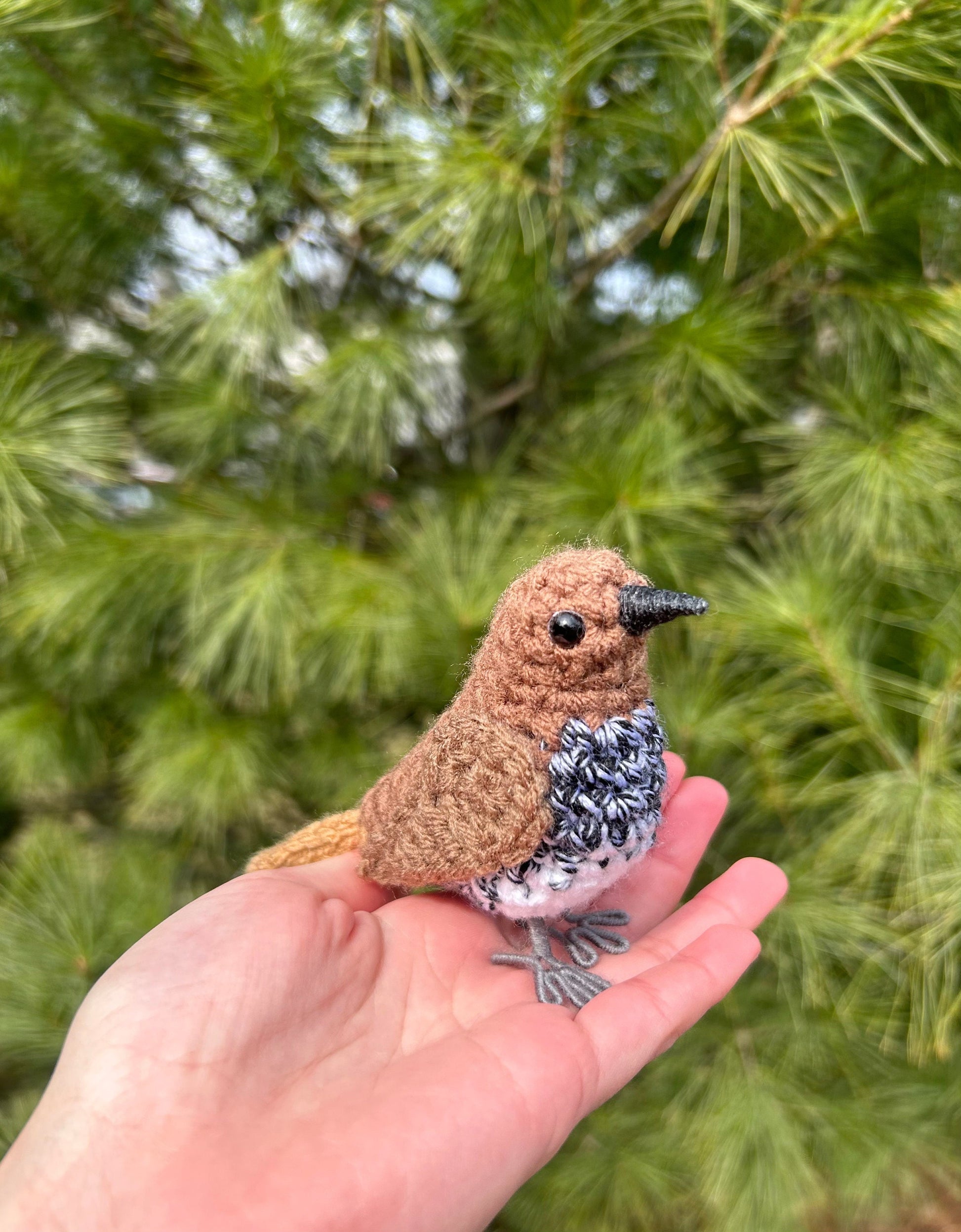 Hand holding a small crocheted bird against a green leafy background