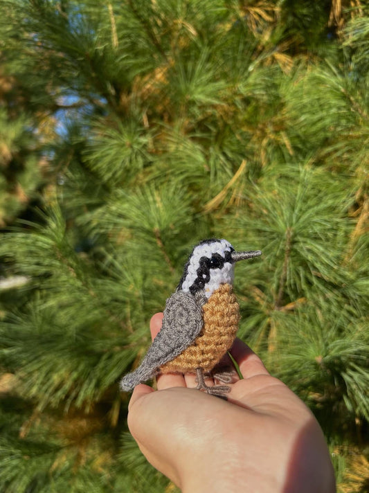 Hand holding a crocheted bird against a green tree background