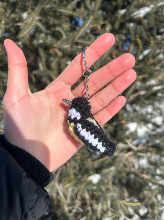 Hand holding a black and white bird-shaped keychain with a snowy background