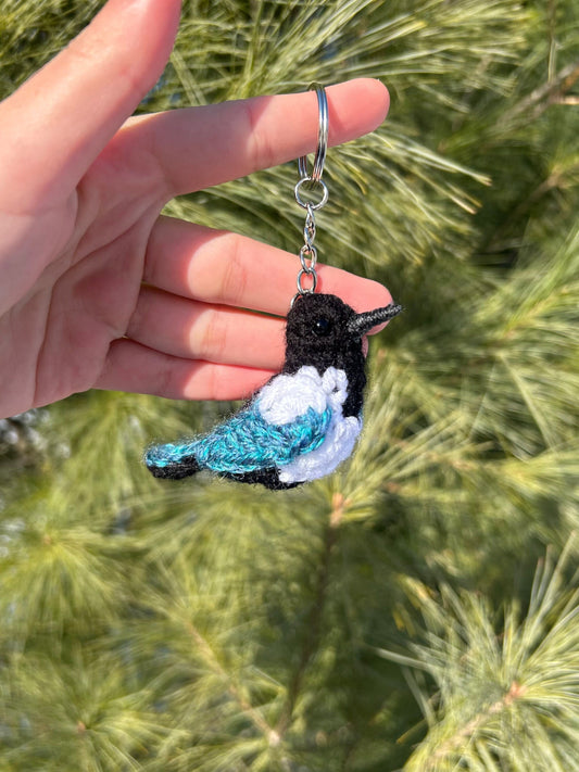 Hand holding a crocheted bird keychain with a green leafy background