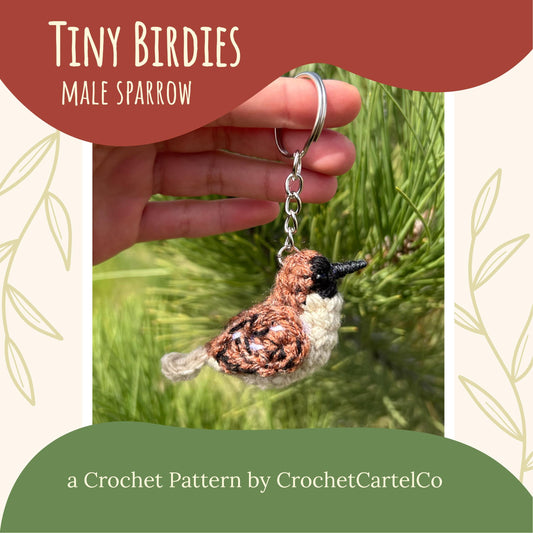 Crocheted bird keychain crochet pattern shown held in a hand with grass background, labeled 'Tiny Birdies Male Sparrow' by CrochetCartelCo.
