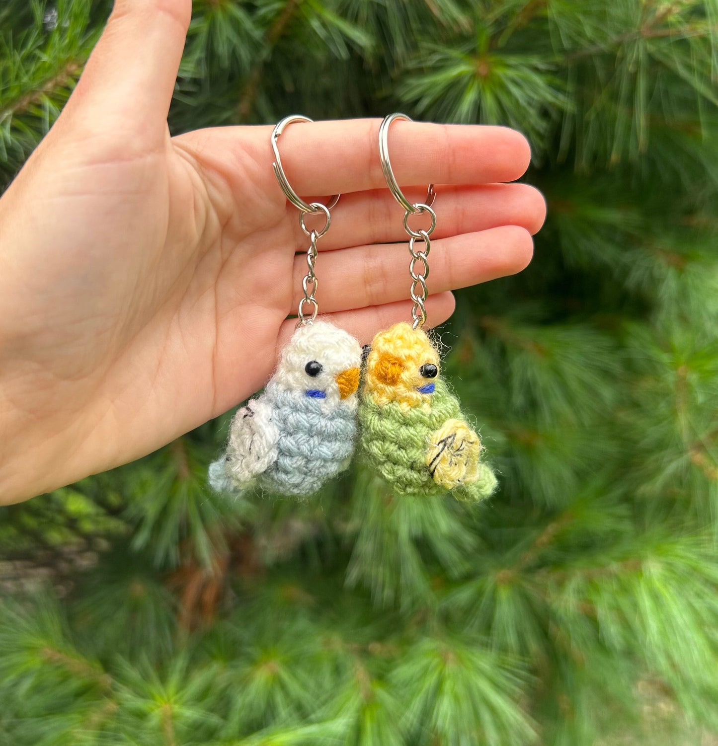 Hand holding two crochet bird keychains against a green leafy background